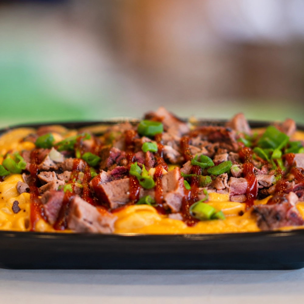 A bowl of mac and cheese topped with brisket, barbecue sauce, green onion, and cilantro